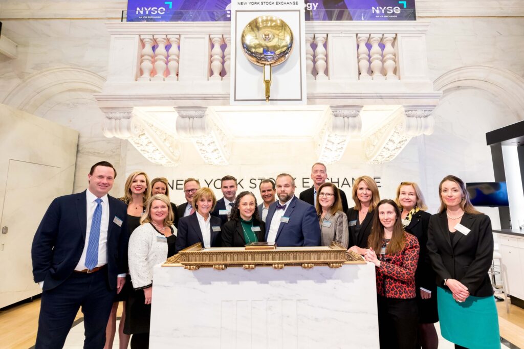 A group of business people standing behind a desk at the New York Stock Exchange bell