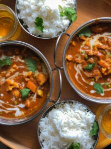 Photo of four bowls on a round serving tray. Two contain white rice and two bowls contain curried vegetables in a sauce