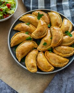 Photo of a platter on a surface containing an arrangement of empanadas.